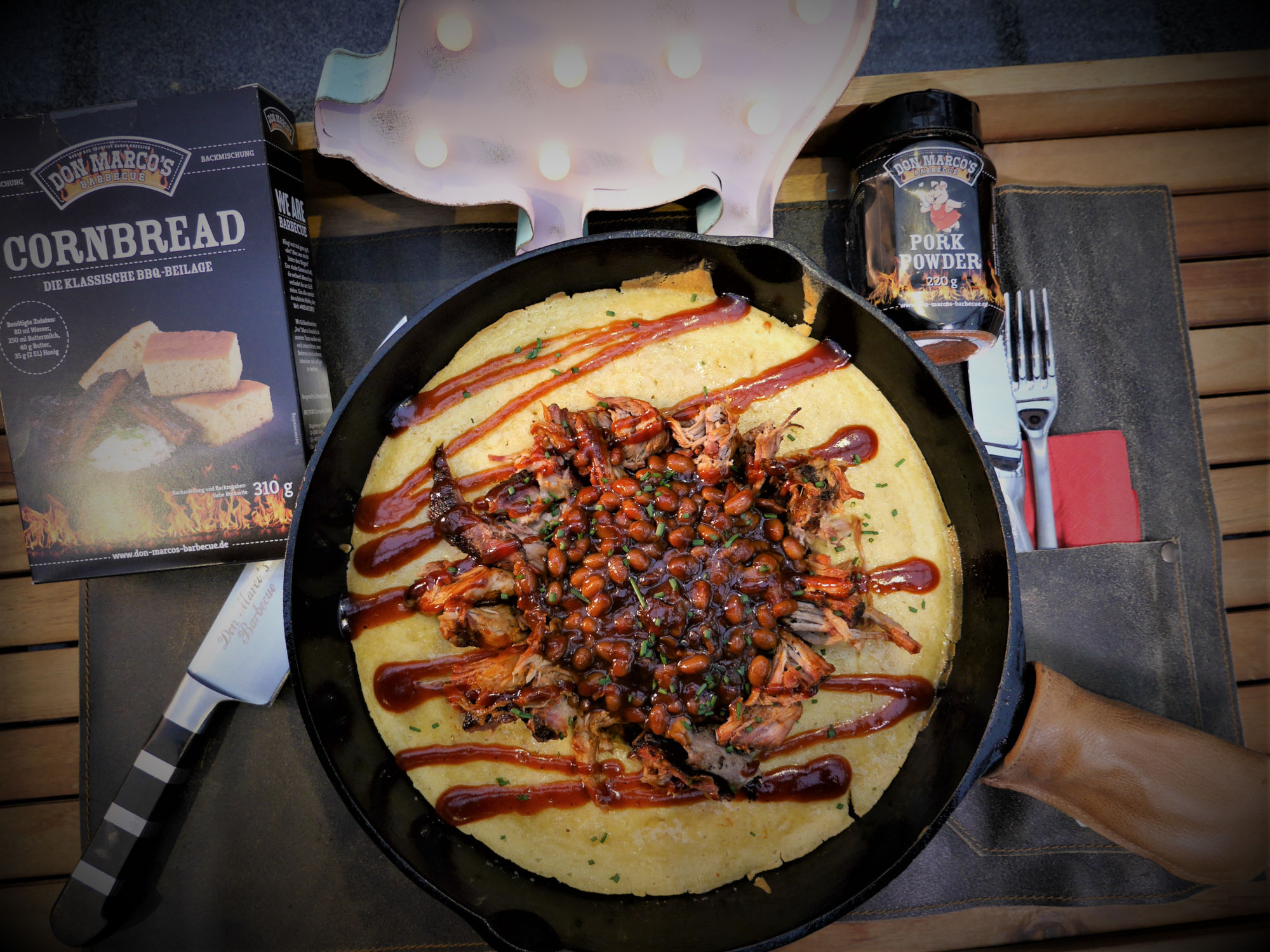 Pulled Pork Cornbread BBQ Beans Pan - Pork Powder Cornbread (10) Pulled Pork auf Cornbread garniert mit BBQ Sauce in Gußpfanne auf Lederschürze
